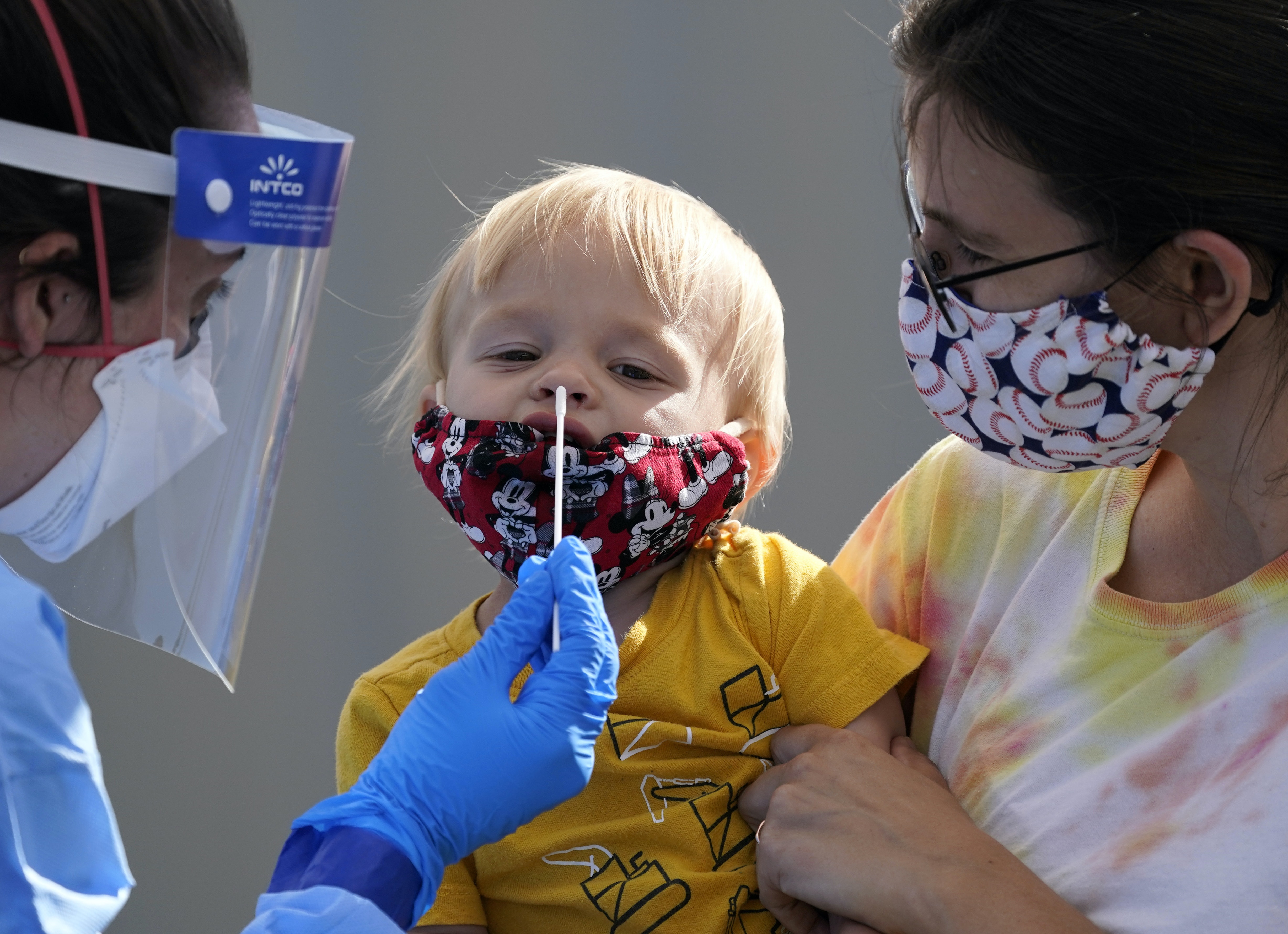 Bei einem sehr kleinen Kind wird von einer medizinischen Fachkraft mit Maske und Gesichtsschutz ein Nasenabstrich auf das Coronavirus durchgeführt