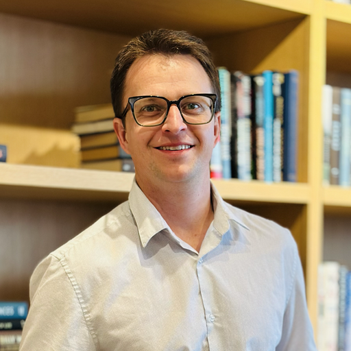 Un hombre con gafas y parado frente a una estantería de libros.